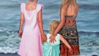 An Oil painting of three sisters standing with their backs to the viewer gazing out to sea standing barefoot at the waters edge. All three sister's have beautiful coloured dresses, in baby pink, turquoise green, orange and black aztec patterned.